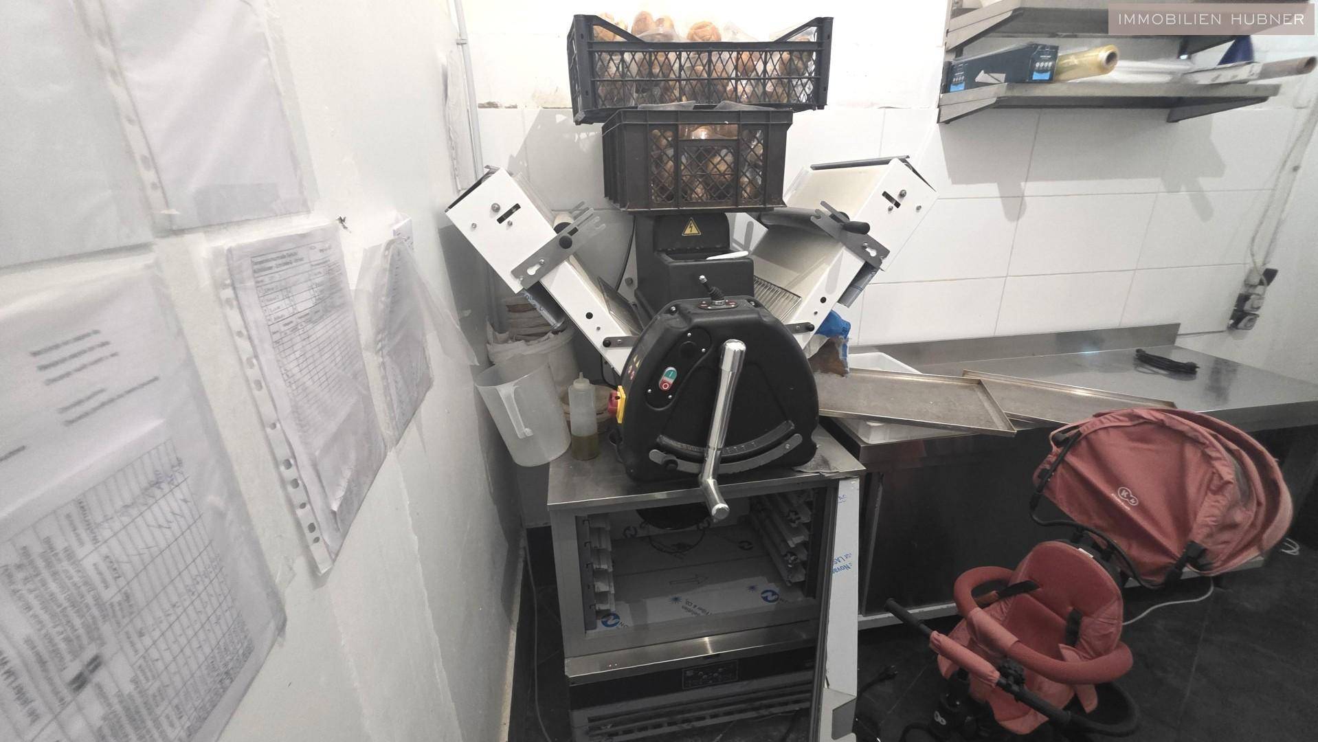 Küchenbereich mit Teigmaschine, Arbeitsflächen und Dokumenten an der Wand.