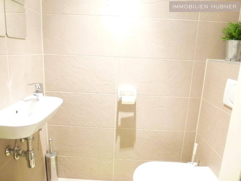 Kleines Gäste-WC mit Wand-WC, Waschbecken und beigefarbenen Fliesen.