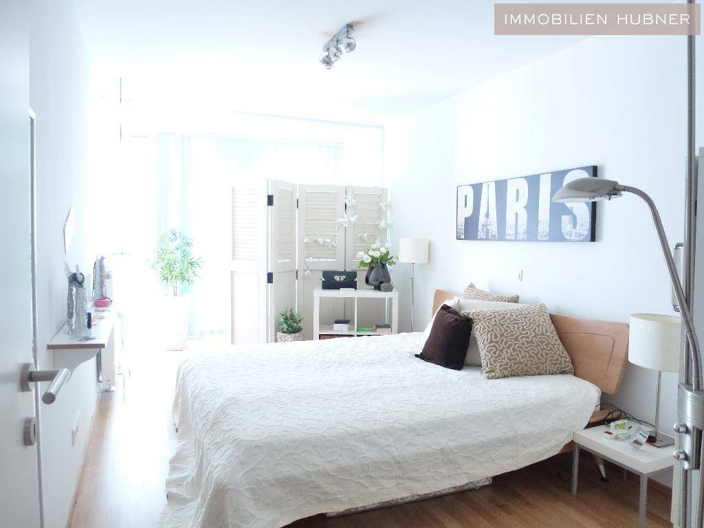 Helles Schlafzimmer mit Doppelbett, Holzboden und Zugang zu einem Balkon oder einer Terrasse.