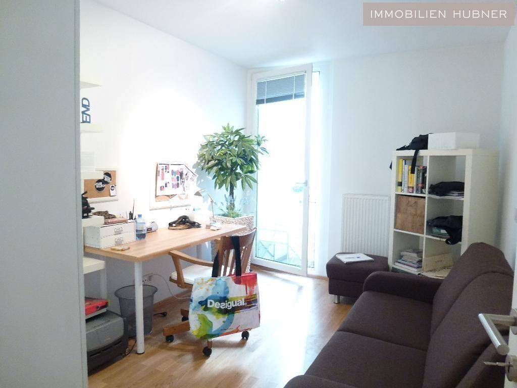 Helles Arbeitszimmer mit Schreibtisch, Regal und Zugang zu einem Außenbereich.