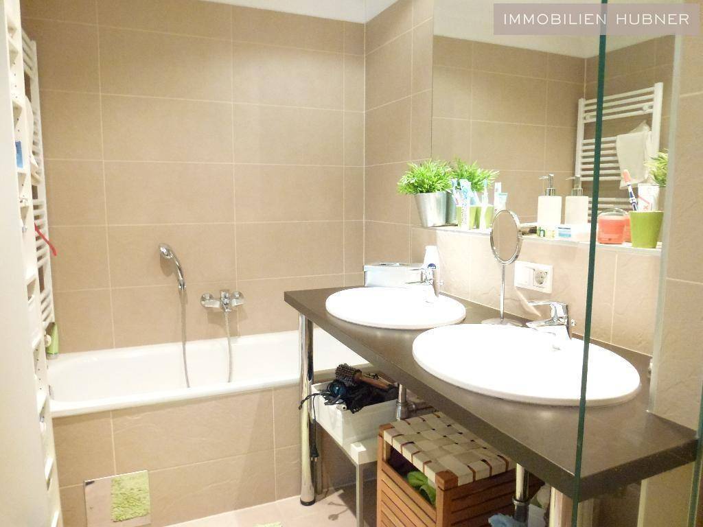 Modernes Badezimmer mit Doppelwaschbecken, Badewanne und beigefarbenen Fliesen.