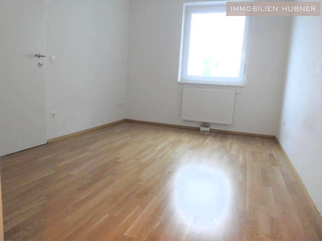 Helles Schlafzimmer mit Parkettboden und einem großen Fenster, das viel Tageslicht hereinlässt.