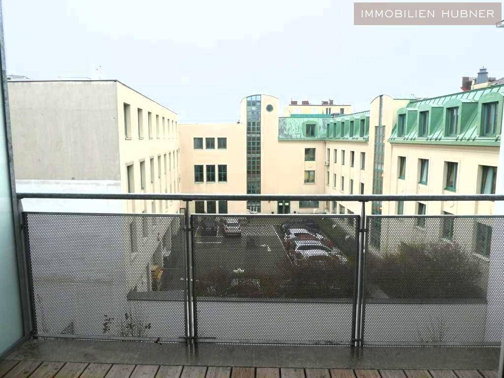 Blick vom Balkon auf einen ruhigen Innenhof mit parkenden Autos und umliegenden Gebäuden.
