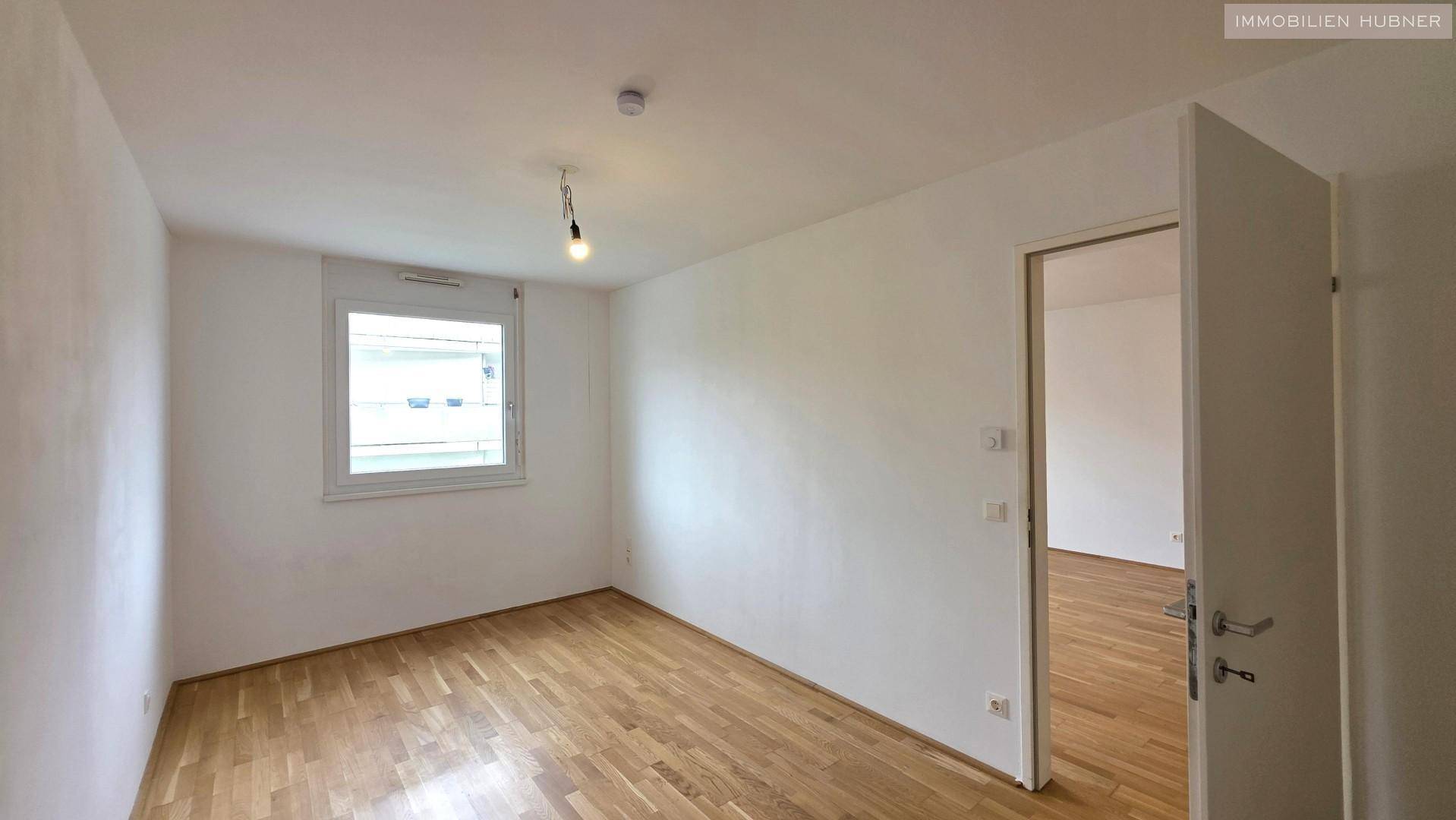 Helles Zimmer mit Parkettboden und einem Fenster, ideal als Schlaf- oder Arbeitszimmer.