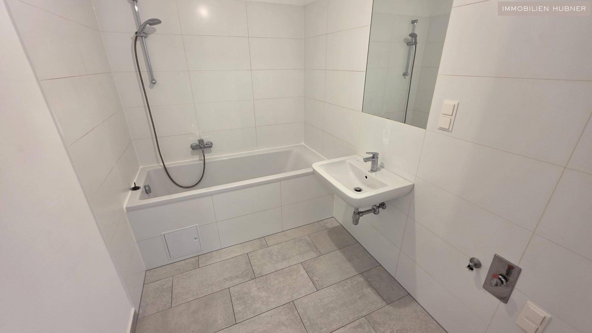 Modernes Badezimmer mit Badewanne, Einzelwaschbecken und weißen Wandfliesen.