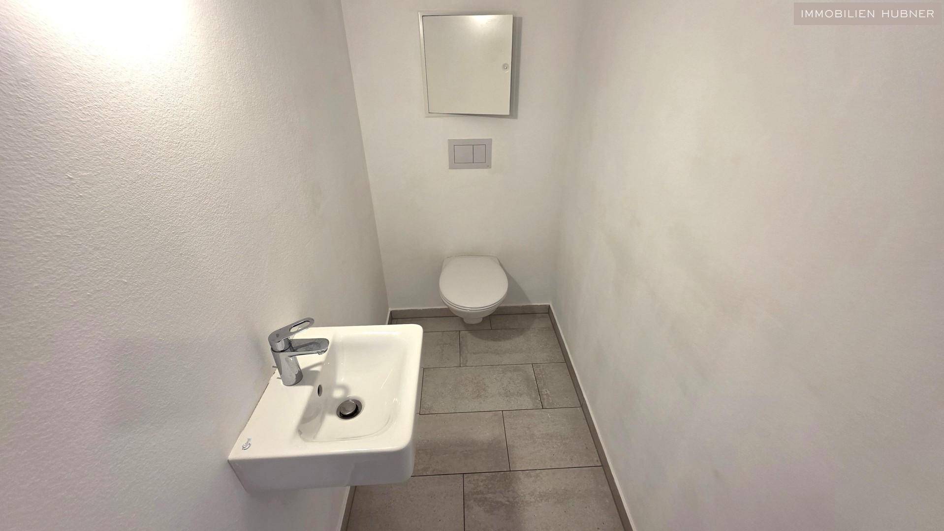 Separates WC mit wandhängender Toilette und kleinem Handwaschbecken.