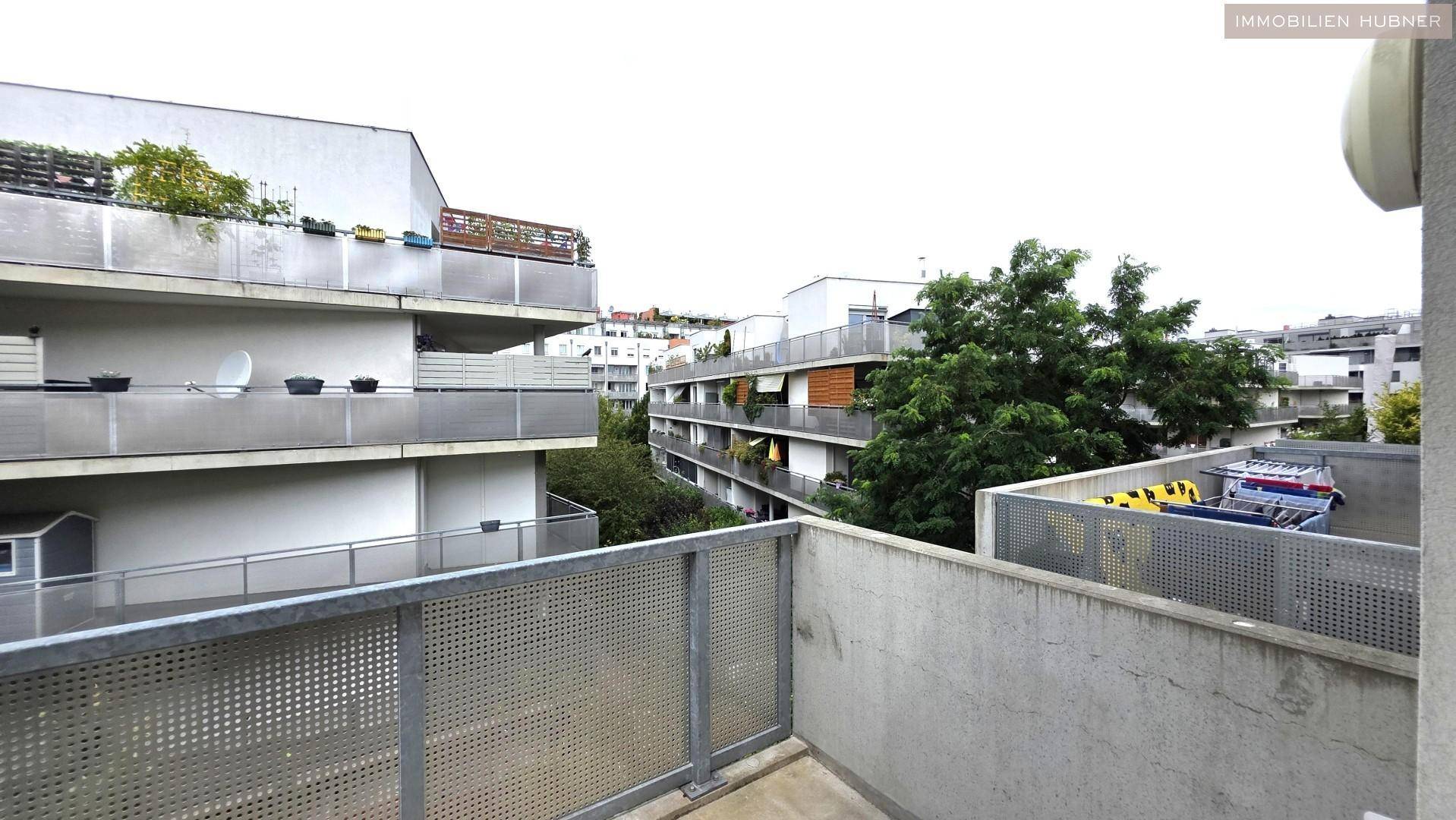 Ausblick von einem Balkon auf umliegende Wohngebäude und grüne Bäume.
