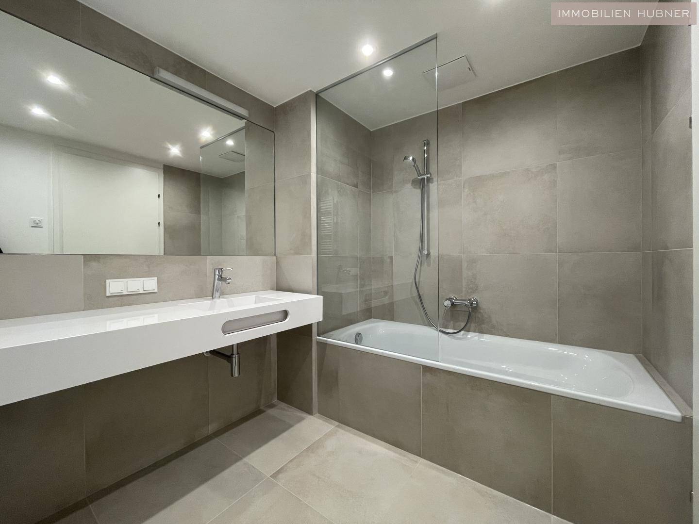 Modernes Badezimmer mit Badewanne, Dusche und großem Waschtisch in neutralen Farbtönen.