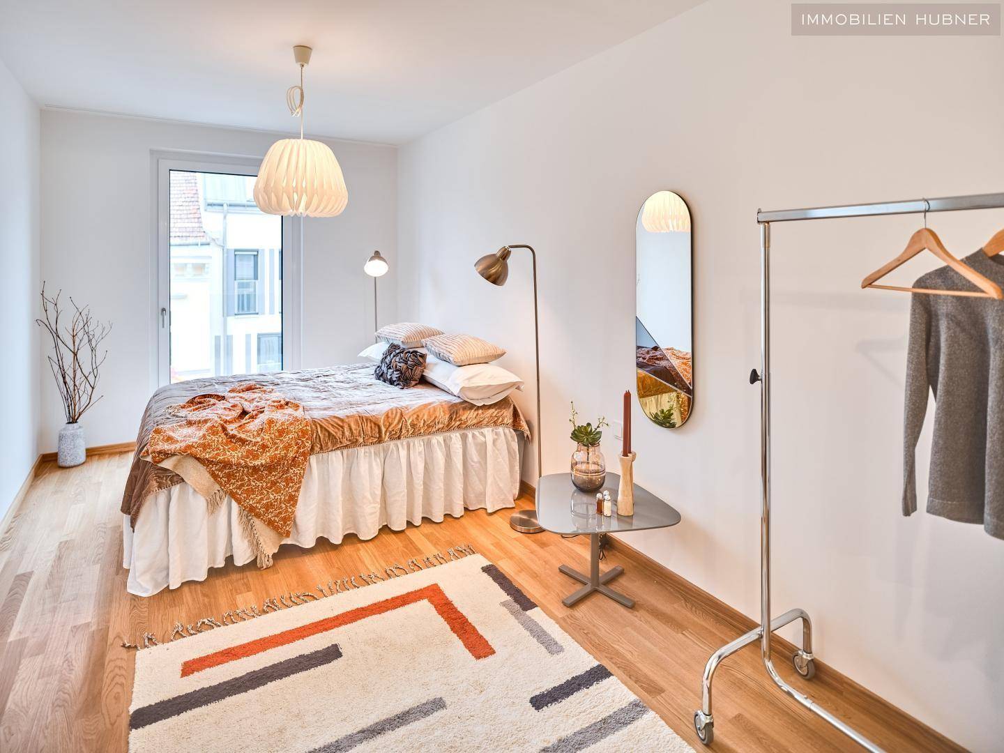 Helles Schlafzimmer mit Parkettboden, großem Fenster und moderner Einrichtung.