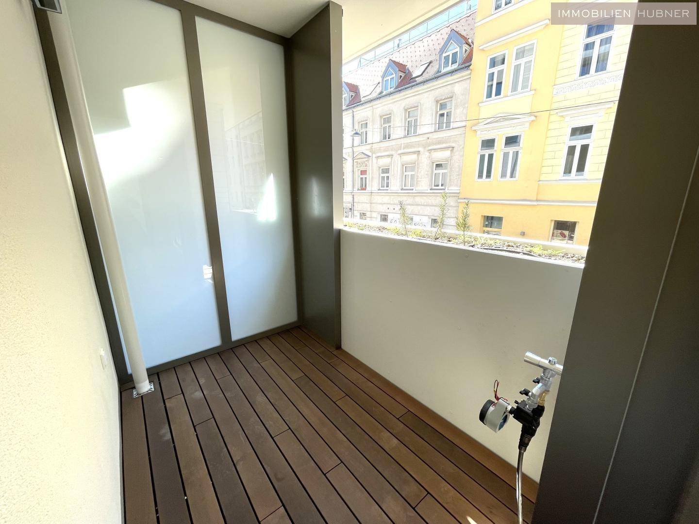 Schmaler Balkon mit Holzboden und Blick auf die umliegenden Gebäude der Stadt.