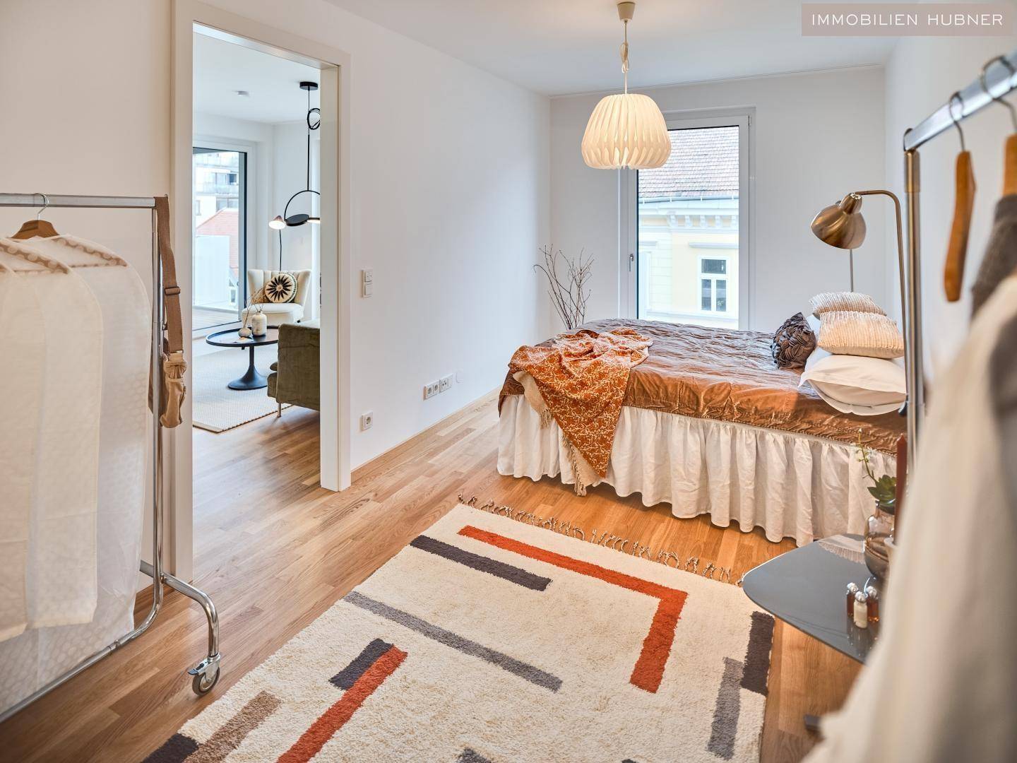 Gemütliches Schlafzimmer mit Parkettboden, Fenster und Blick in den Wohnbereich.