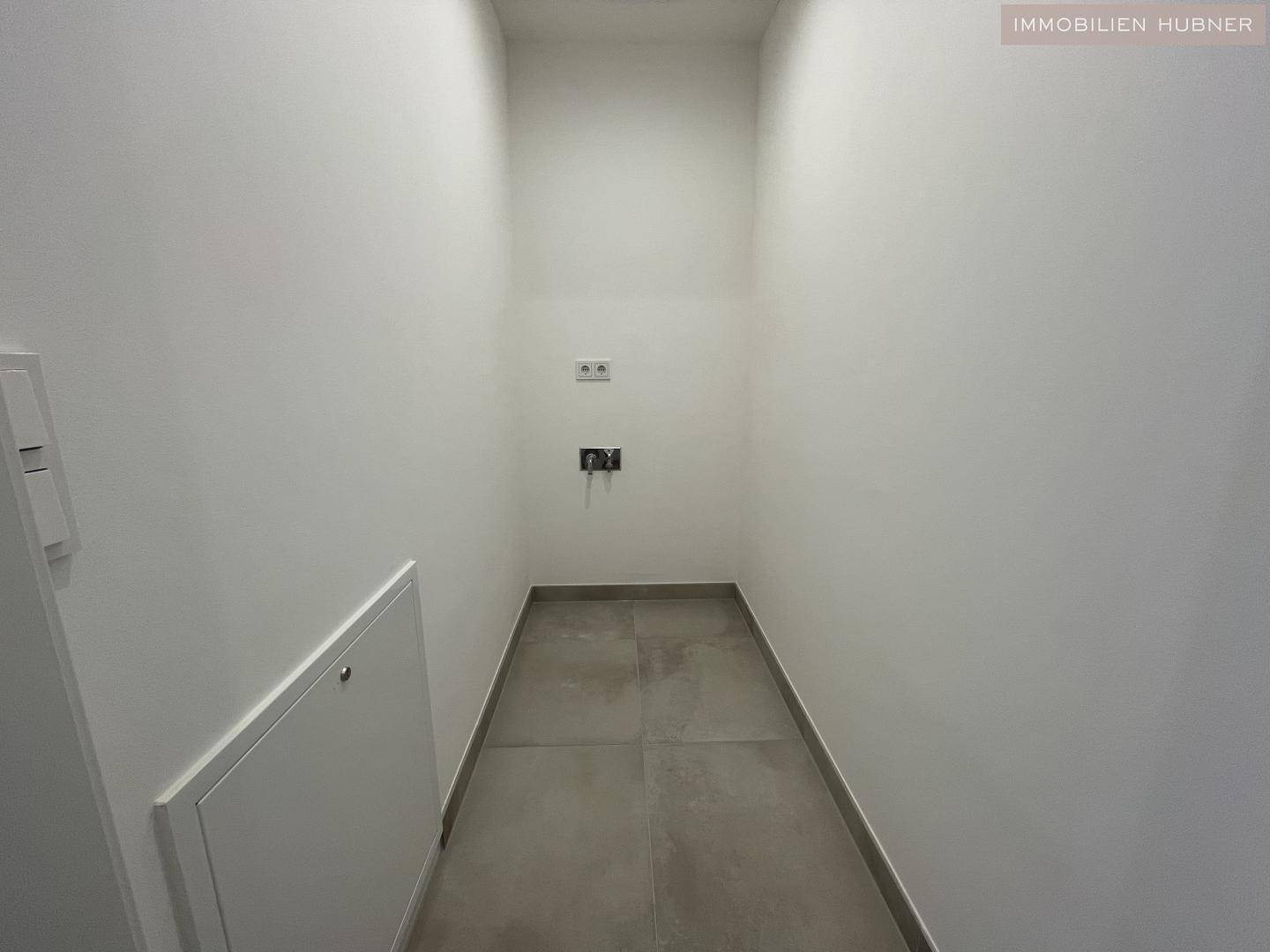 Praktischer Abstellraum mit Fliesenboden und Anschlüssen für Waschmaschine und Trockner.