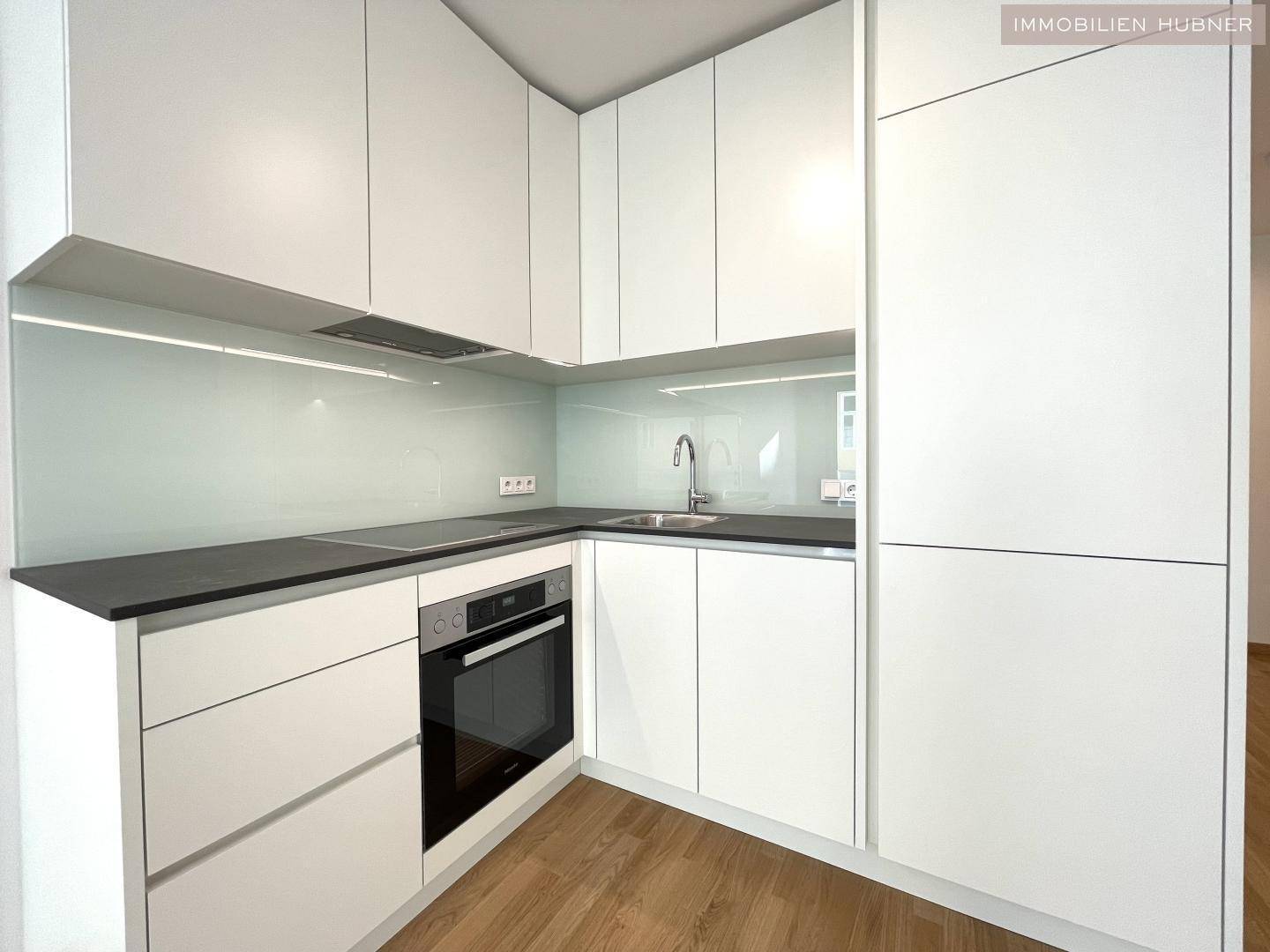 Moderne Einbauküche mit weißen Schränken, dunkler Arbeitsplatte und integrierten Geräten.