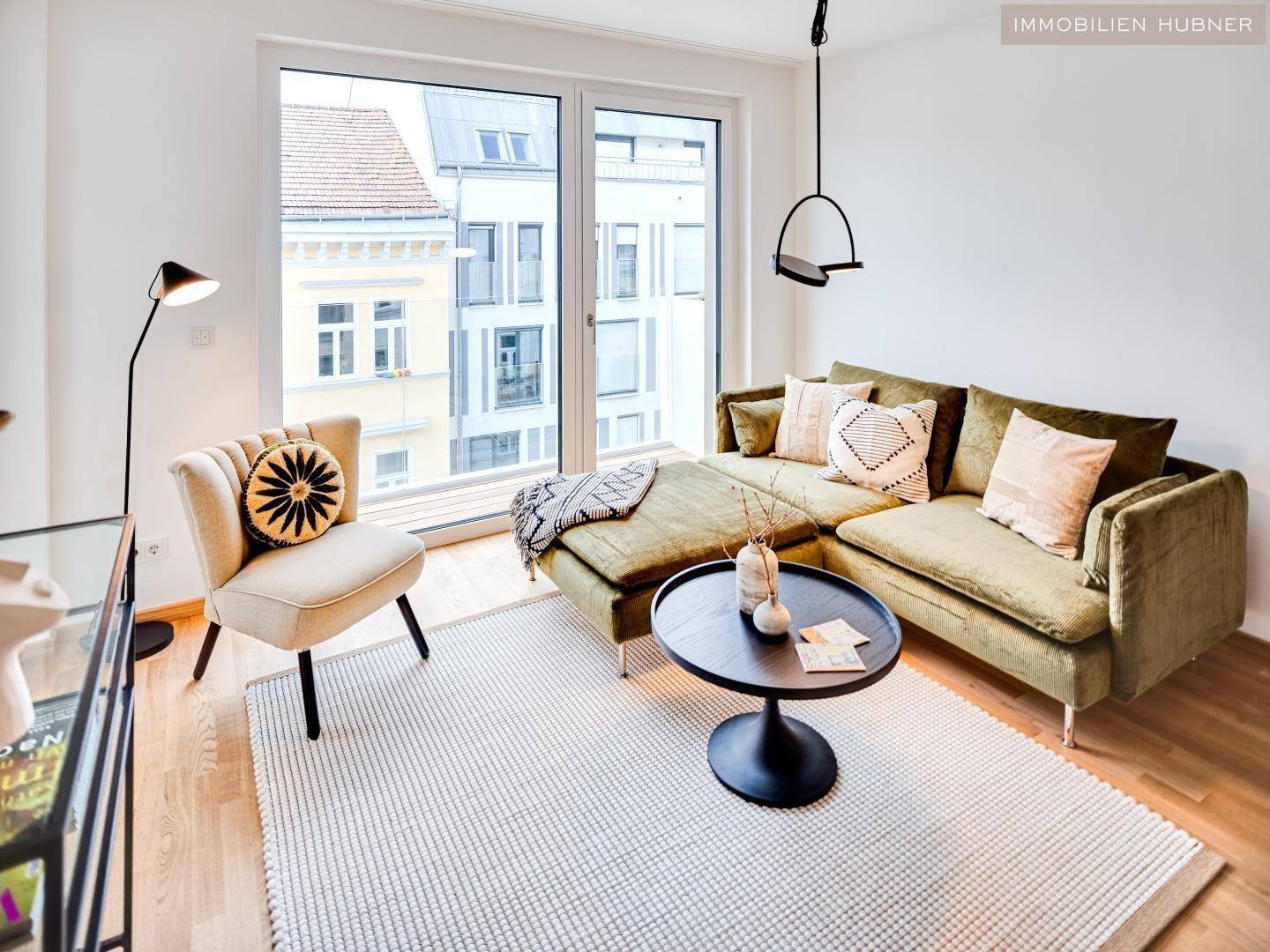 Heller Wohnbereich mit bequemer Couch, Teppich und großen Fenstern mit Stadtblick.
