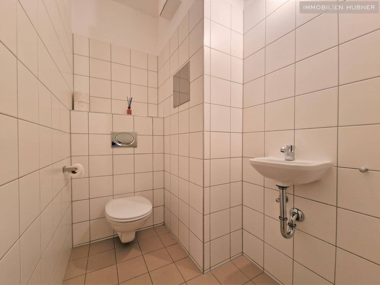 Separates WC mit wandhängender Toilette und kleinem Handwaschbecken, komplett gefliest.