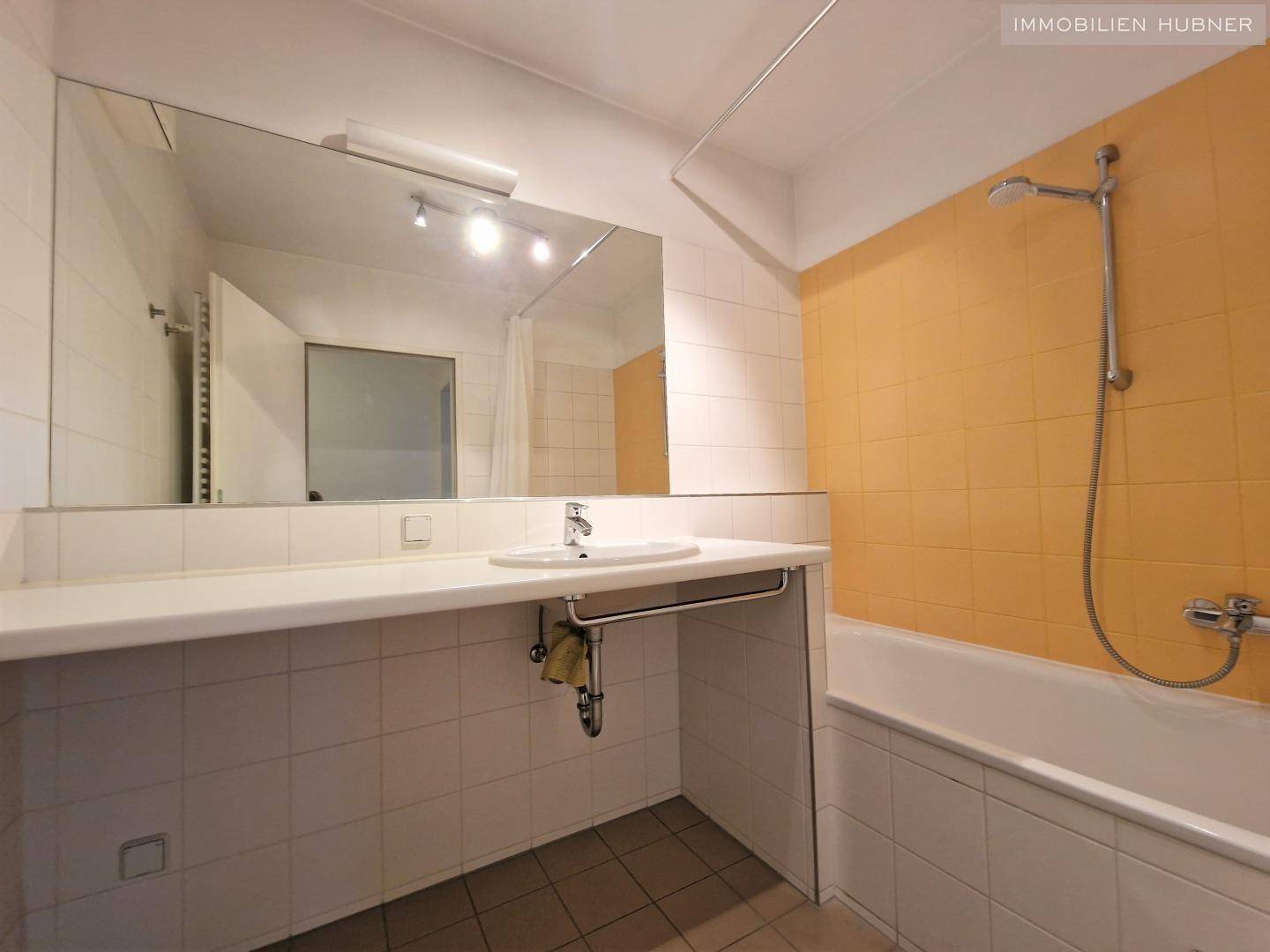 Badezimmer mit Badewanne, Waschbecken und großen Spiegeln, teilweise orange gefliest.