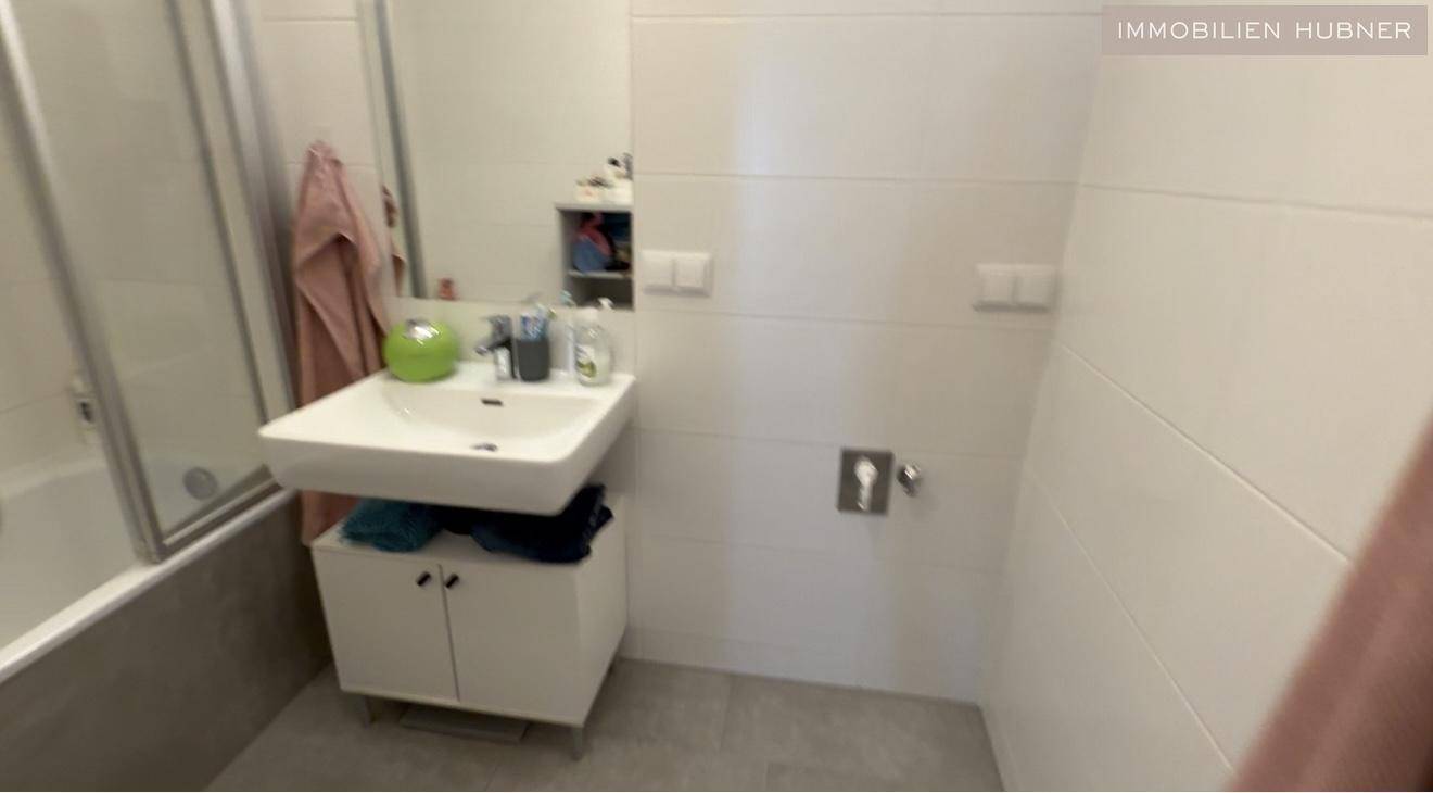 Badezimmer mit Badewanne, Duschabtrennung und modernem Waschtisch.