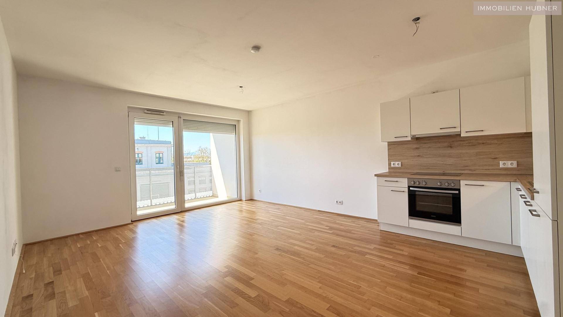 Heller Wohnbereich mit offener Küche, Parkettboden und Zugang zum Balkon.