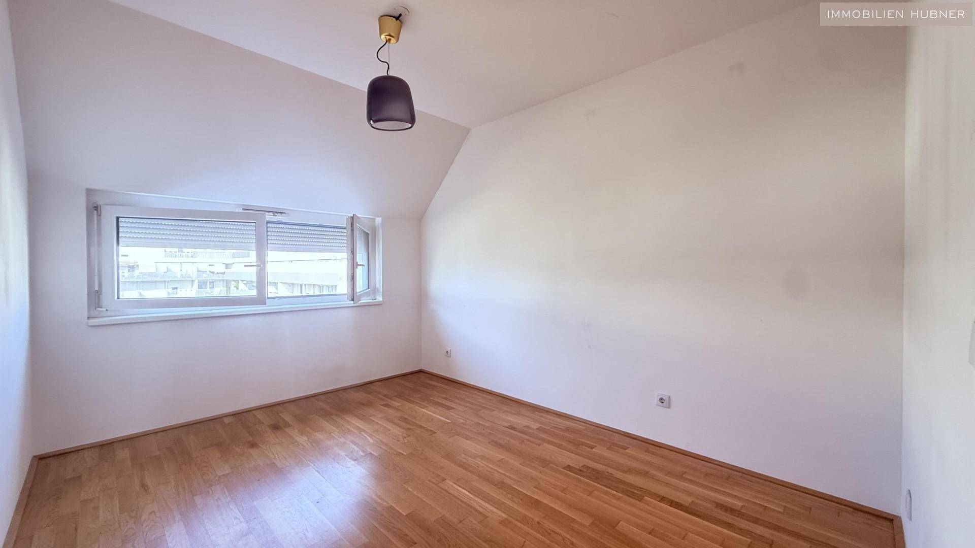 Weiteres Schlafzimmer mit Parkettboden, Dachschräge und Fenster mit Rollladen.
