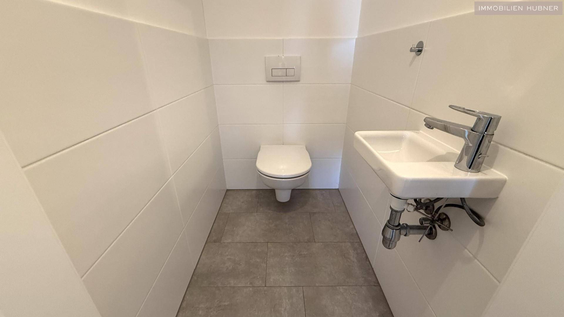 Separates Gäste-WC mit Wand-WC und kleinem Waschbecken, modern gefliest.