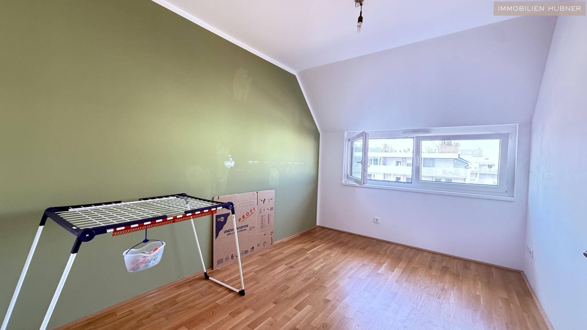 Schlafzimmer mit Dachschräge, Parkettboden und einem Fenster mit Blick nach draußen.
