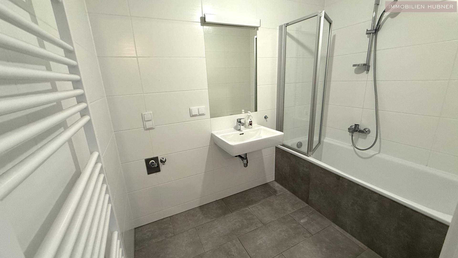 Modernes Badezimmer mit Badewanne, Dusche und beheiztem Handtuchhalter.