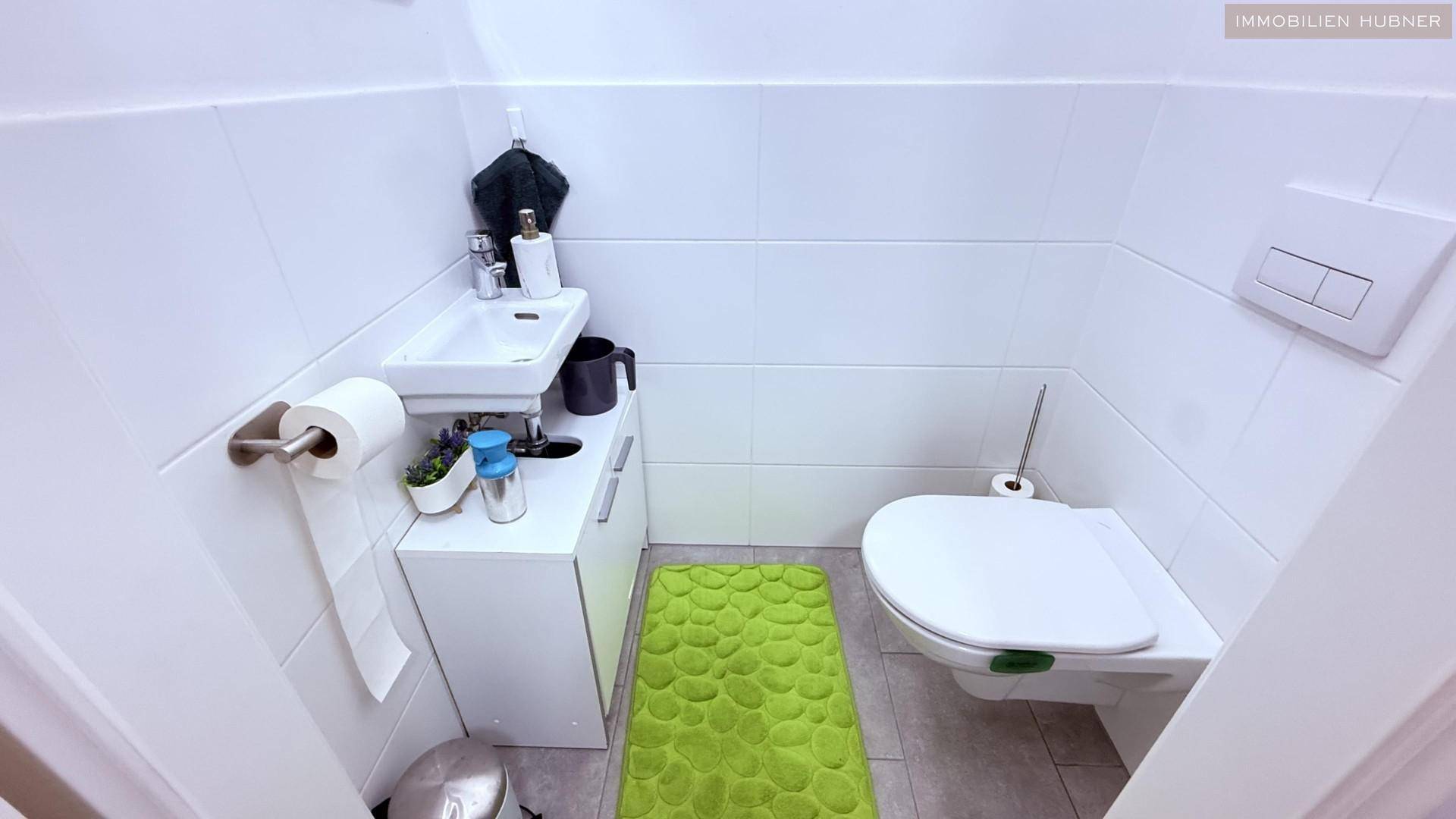 Kleines Gäste-WC mit wandhängendem WC, Handwaschbecken und Fliesenboden.