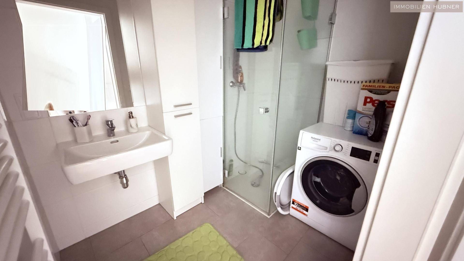 Modernes Badezimmer mit Dusche, Waschbecken, Spiegelschrank und Waschmaschine.