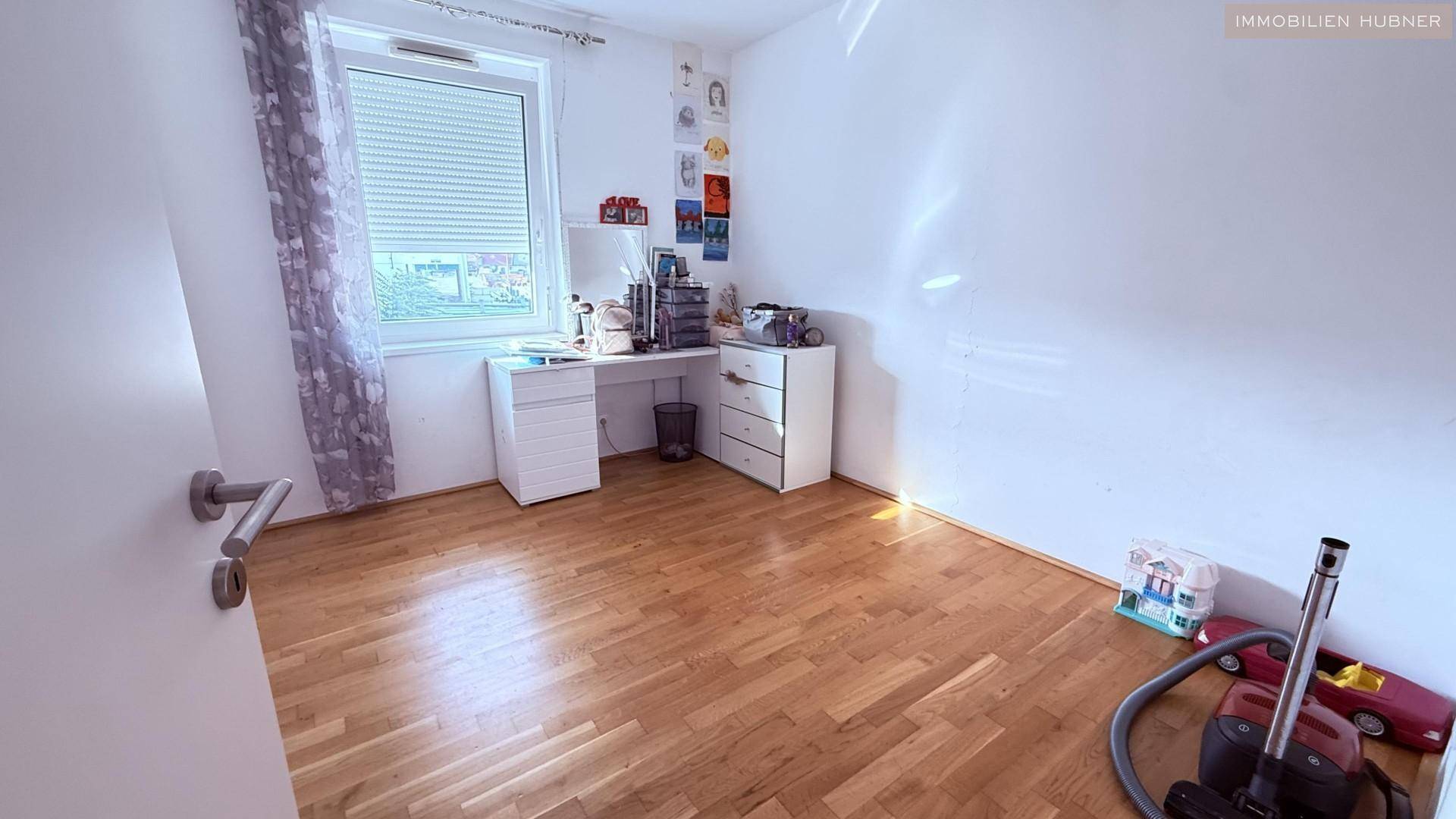 Helles Schlafzimmer mit Parkettboden, großem Fenster und ausreichend Platz für Möbel.