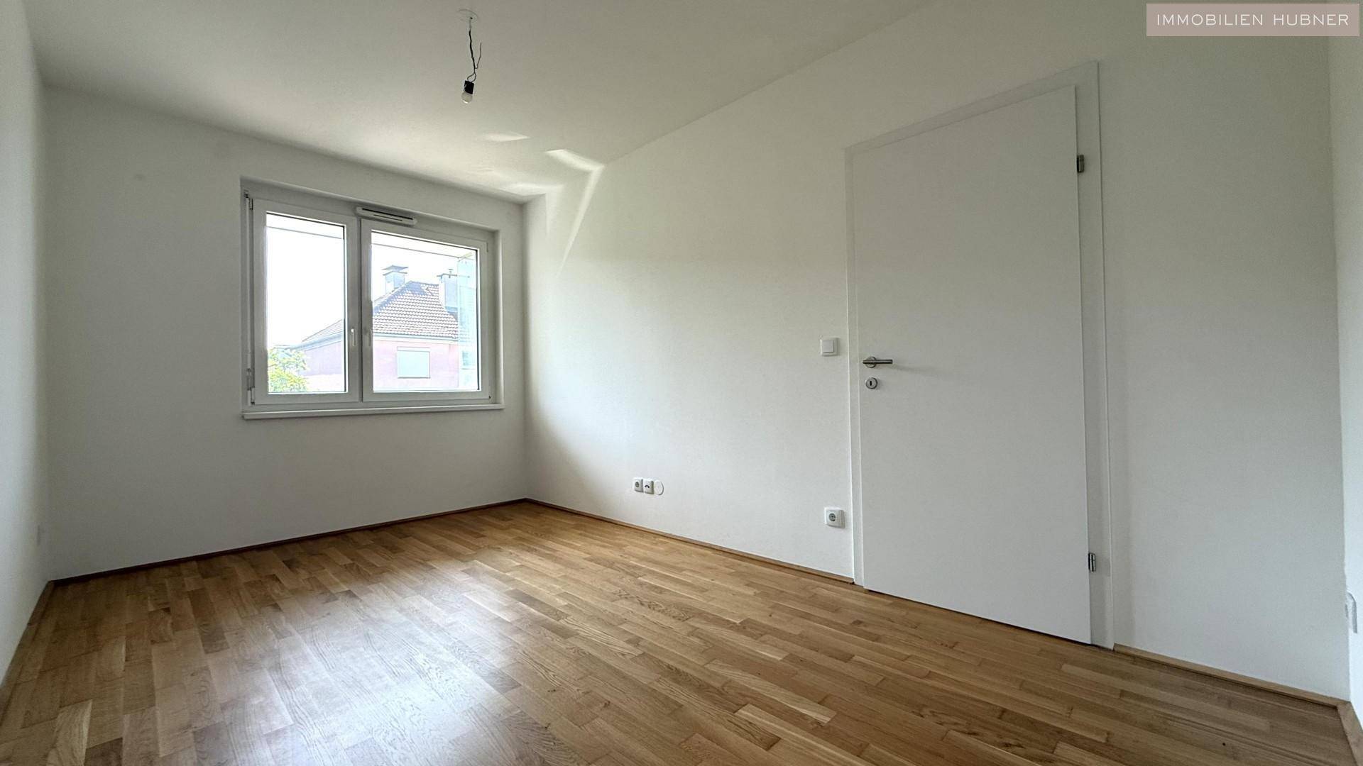 Helles Schlafzimmer mit Parkettboden und großem Fenster, bereit zur individuellen Gestaltung.