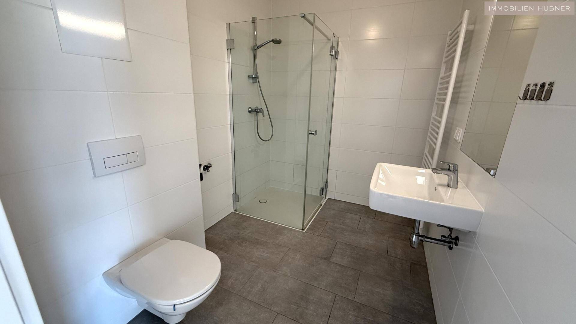 Modernes Badezimmer mit Duschkabine, wandhängendem WC und Handtuchheizkörper.