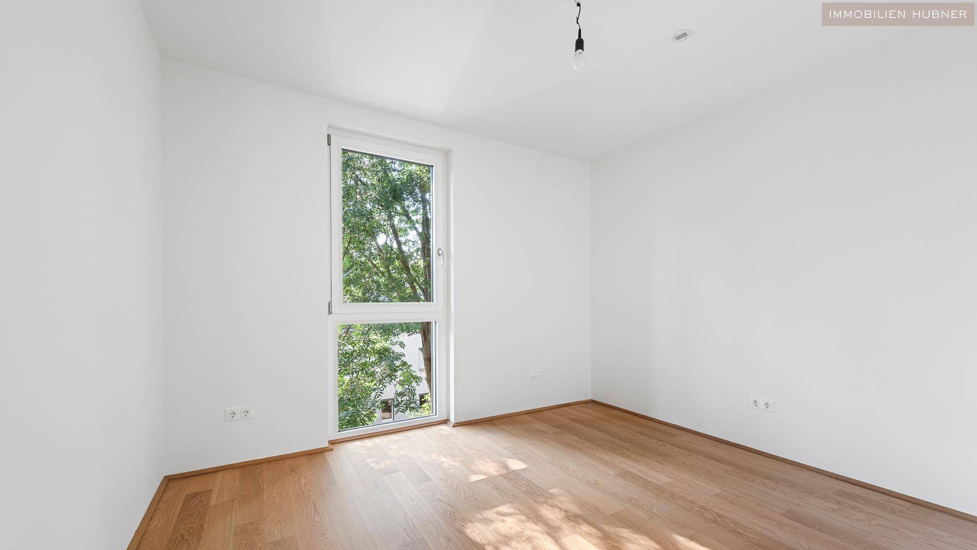 Geräumiges Zimmer mit Holzboden und viel Tageslicht durch das große Fenster.