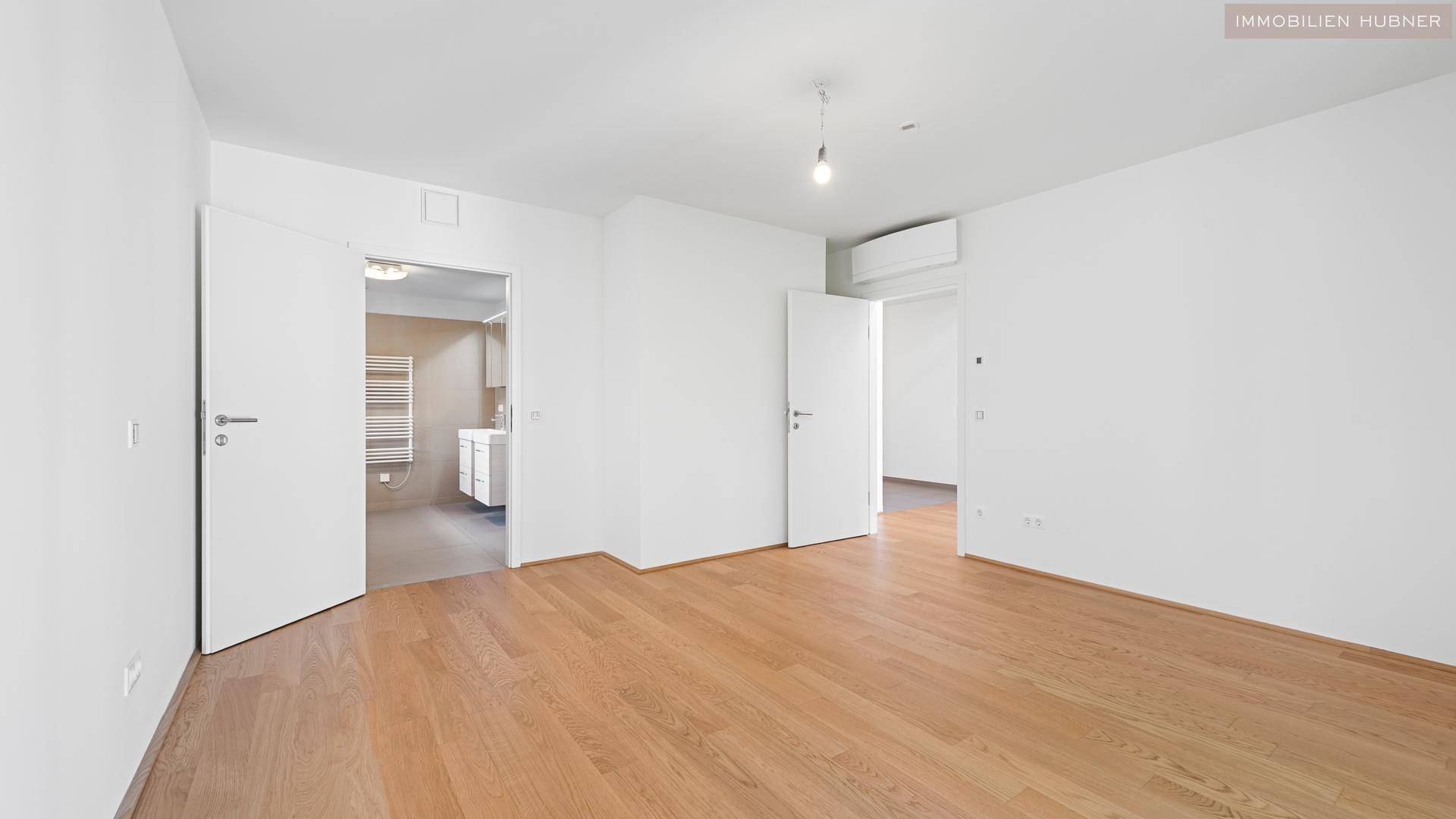 Geräumiges Zimmer mit Holzboden und Zugang zu einem modernen Badezimmer.