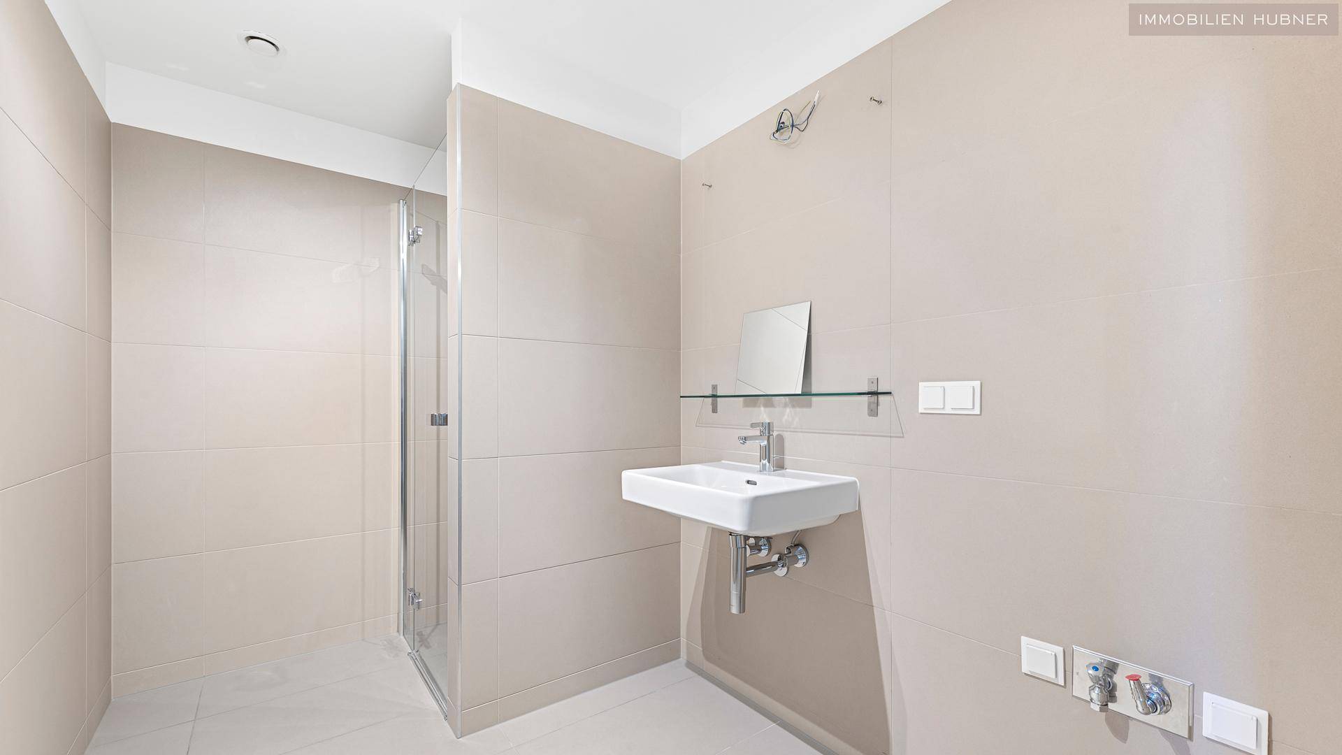 Modernes Badezimmer mit ebenerdiger Dusche und Waschbecken in neutralen Farbtönen.