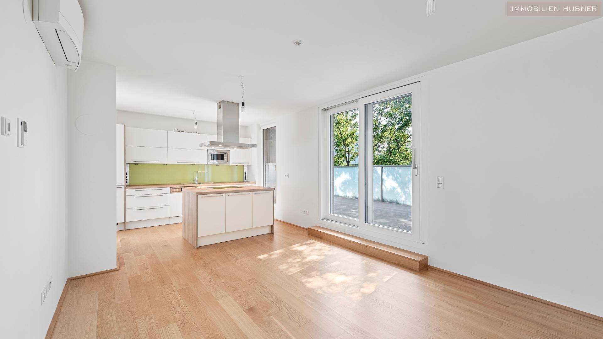Geräumiger Wohnbereich mit offener Küche, Holzboden und Zugang zur Terrasse.