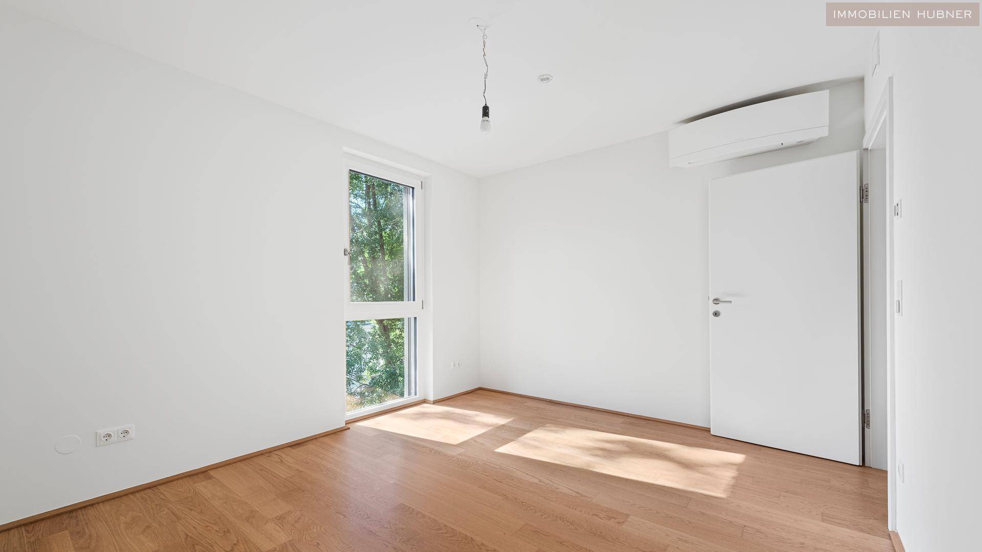 Helles Schlafzimmer mit Holzboden, Klimaanlage und großem Fenster.