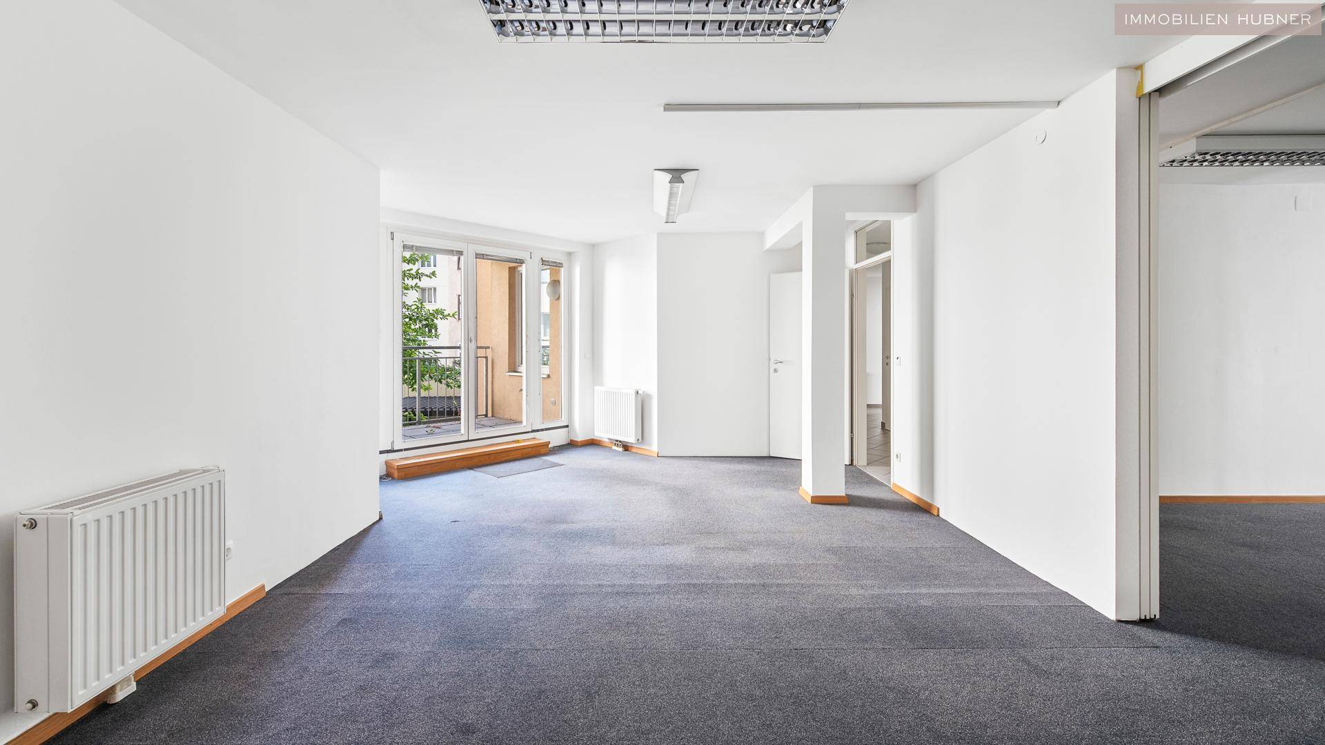 Großer, heller Büroraum mit Teppichboden und Zugang zu einem Balkon, der viel Tageslicht bietet.