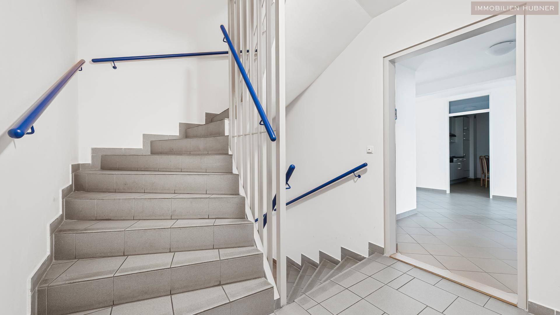 Treppenhaus mit Fliesenstufen und blauem Handlauf, das die verschiedenen Etagen erschließt.
