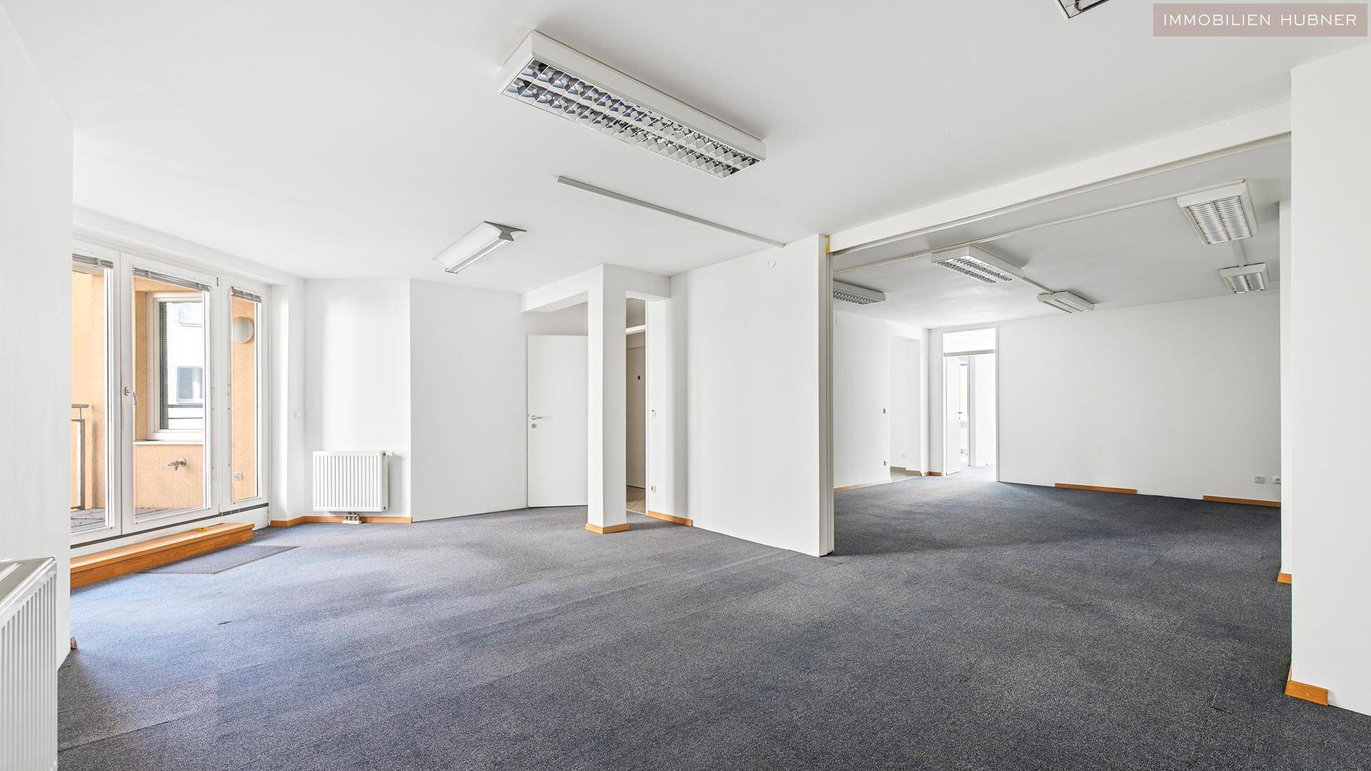 Weitläufiger Bürobereich mit Teppichboden und mehreren Fenstern, die für eine helle Atmosphäre sorgen.
