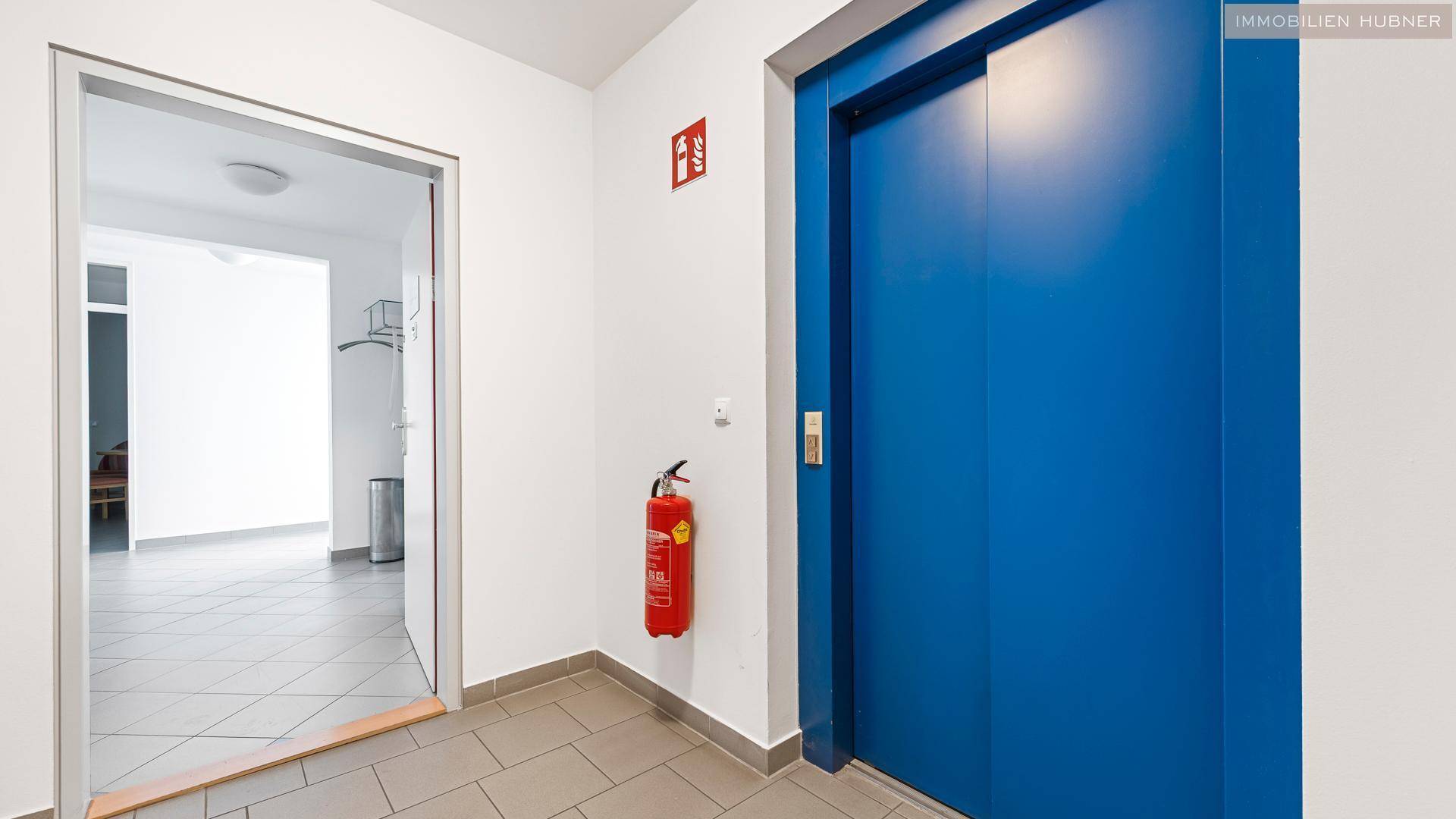 Eingangsbereich mit Fliesenboden und einem blauen Aufzug, der die Etagen verbindet.