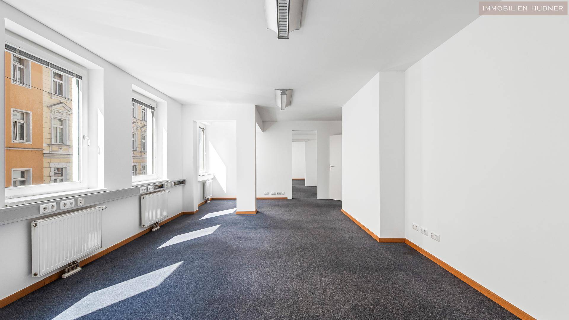 Heller Büroraum mit Teppichboden und großen Fenstern, die für eine angenehme Arbeitsatmosphäre sorgen.