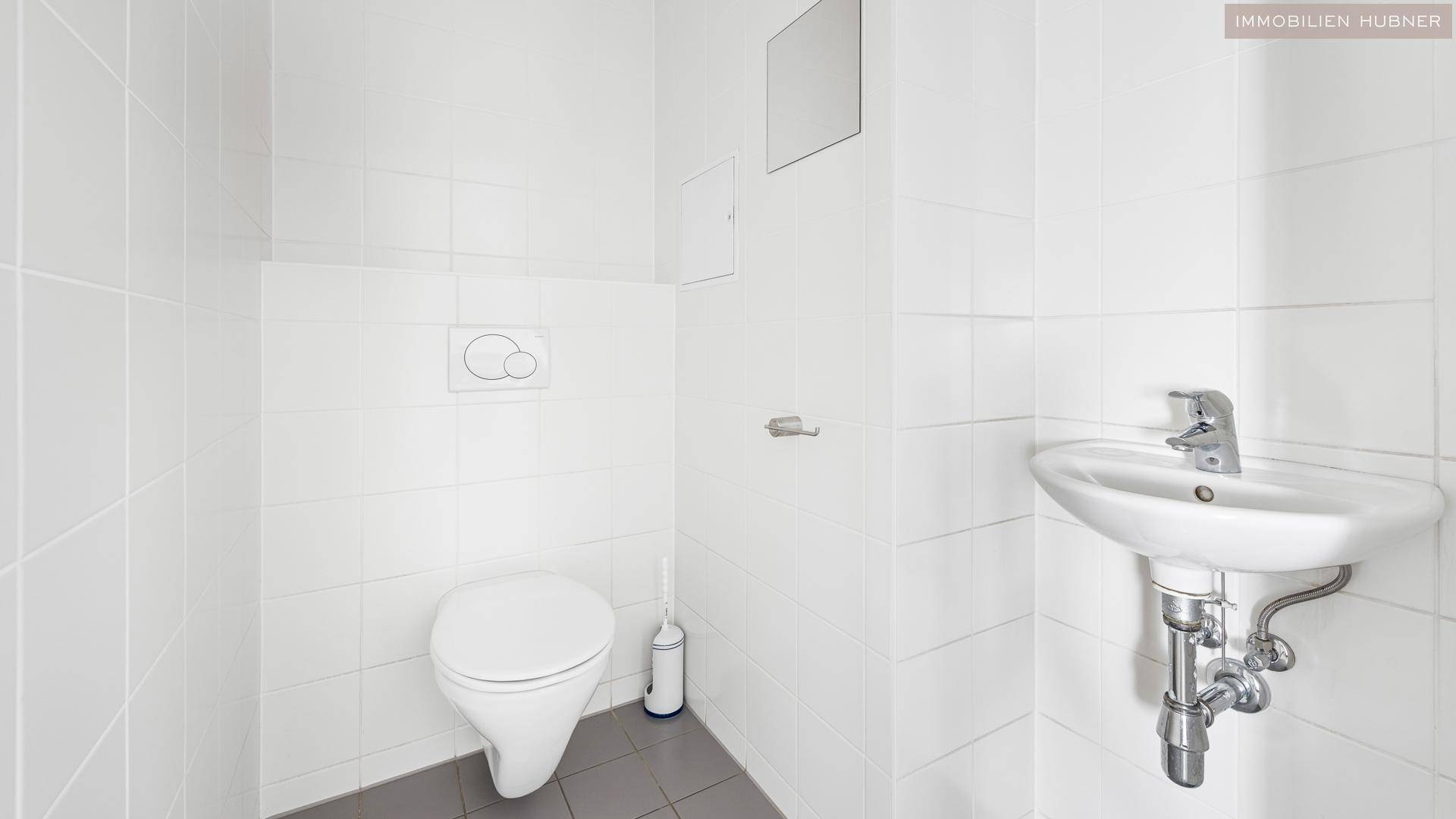 Separate Toilette mit Waschbecken und Fliesenboden, die einen gepflegten Eindruck macht.