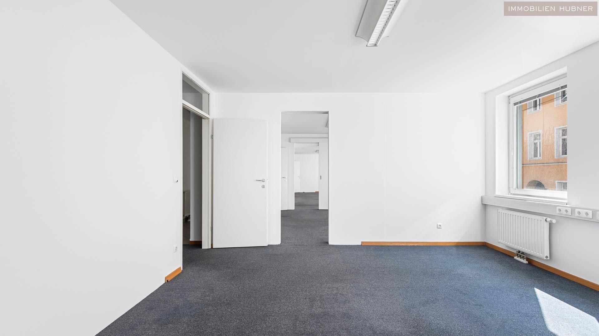 Geräumiger Büroraum mit Teppichboden und mehreren Türen, die zu weiteren Bereichen führen.