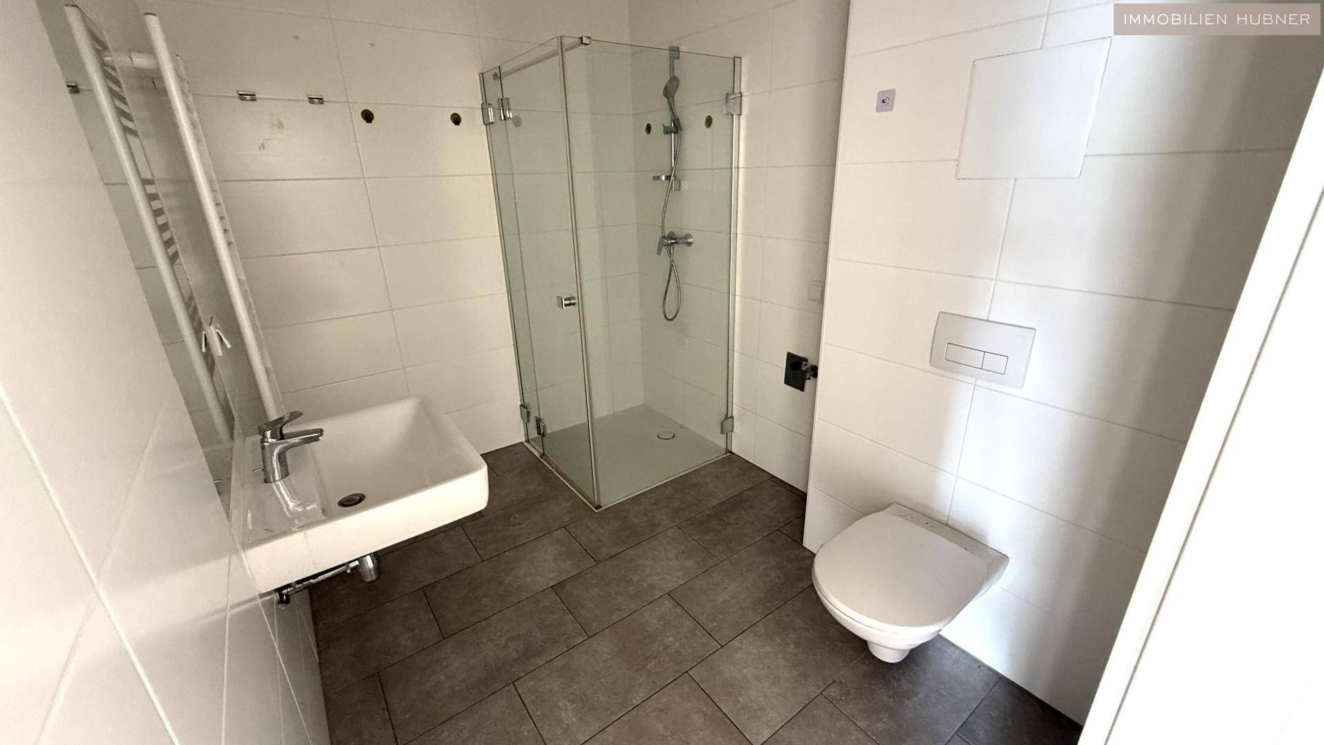 Modernes Badezimmer mit Duschkabine, Wand-WC, Waschbecken und weißen Fliesen.