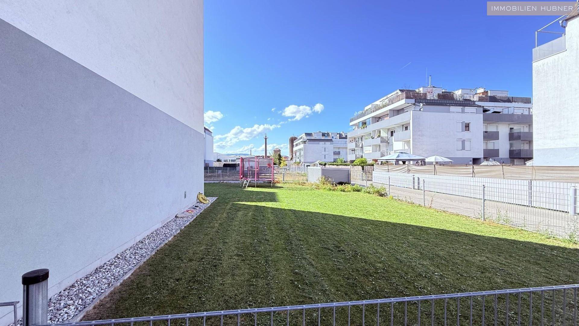 Gepflegter Rasenbereich neben einem Wohngebäude mit Blick auf weitere Neubauten.