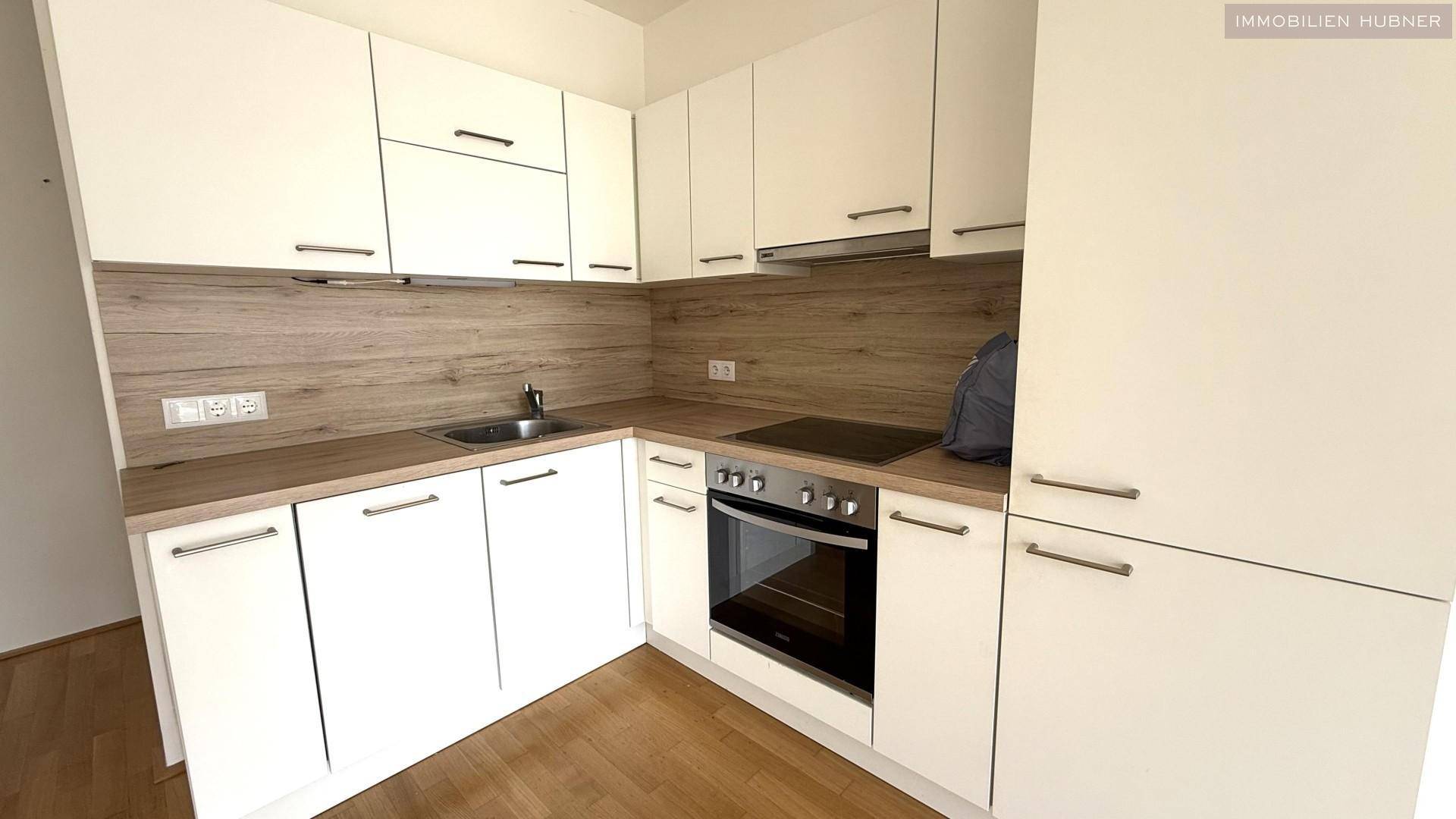Moderne Einbauküche mit weißen Fronten, Holzoptik-Arbeitsplatte und integriertem Backofen.