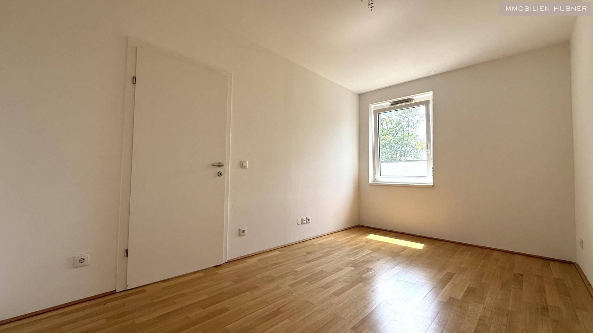 Helles Schlafzimmer mit Parkettboden und einem Fenster, das viel Tageslicht hereinlässt.