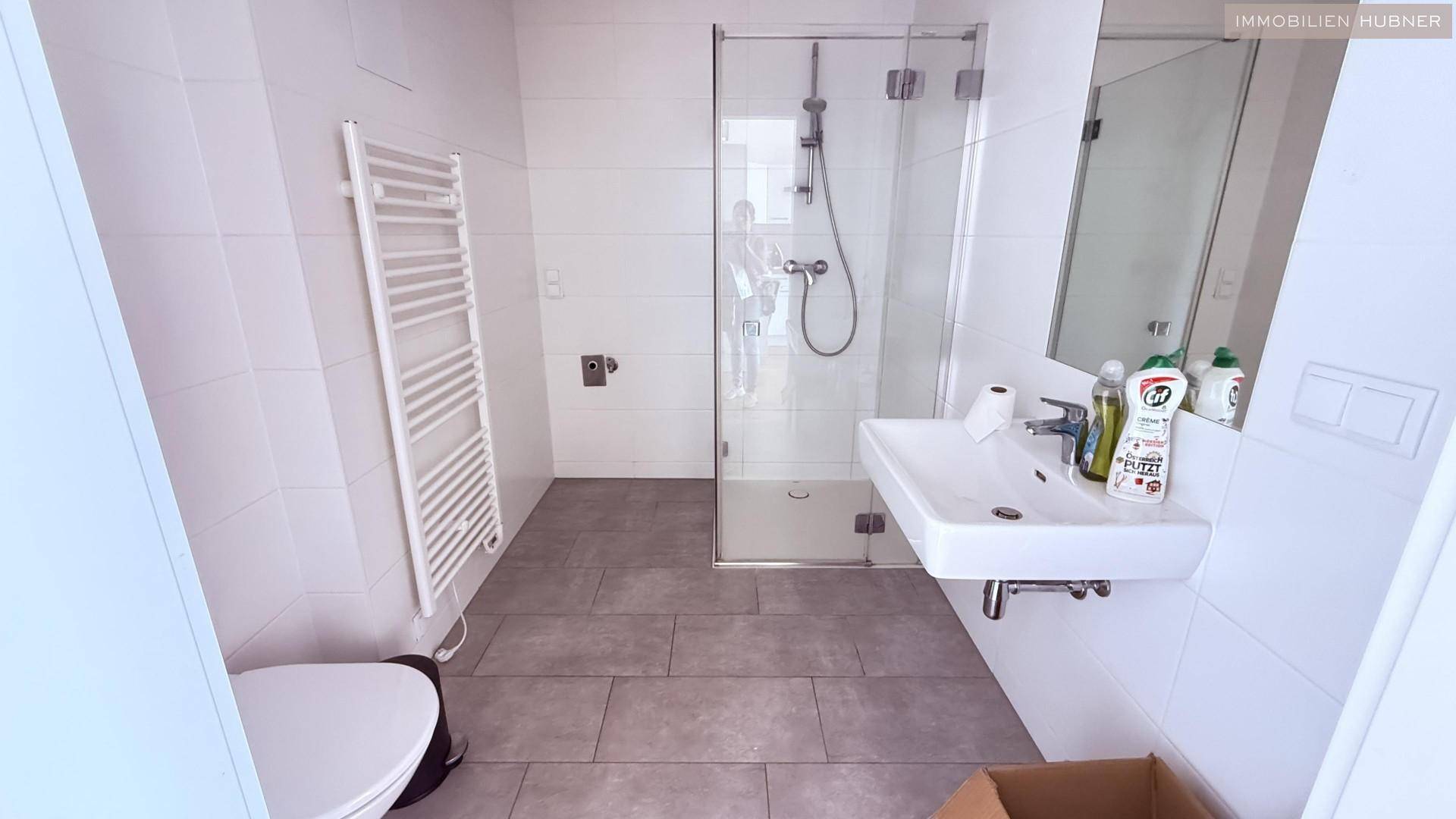 Modernes Badezimmer mit Dusche, Waschbecken, WC und beheiztem Handtuchhalter.