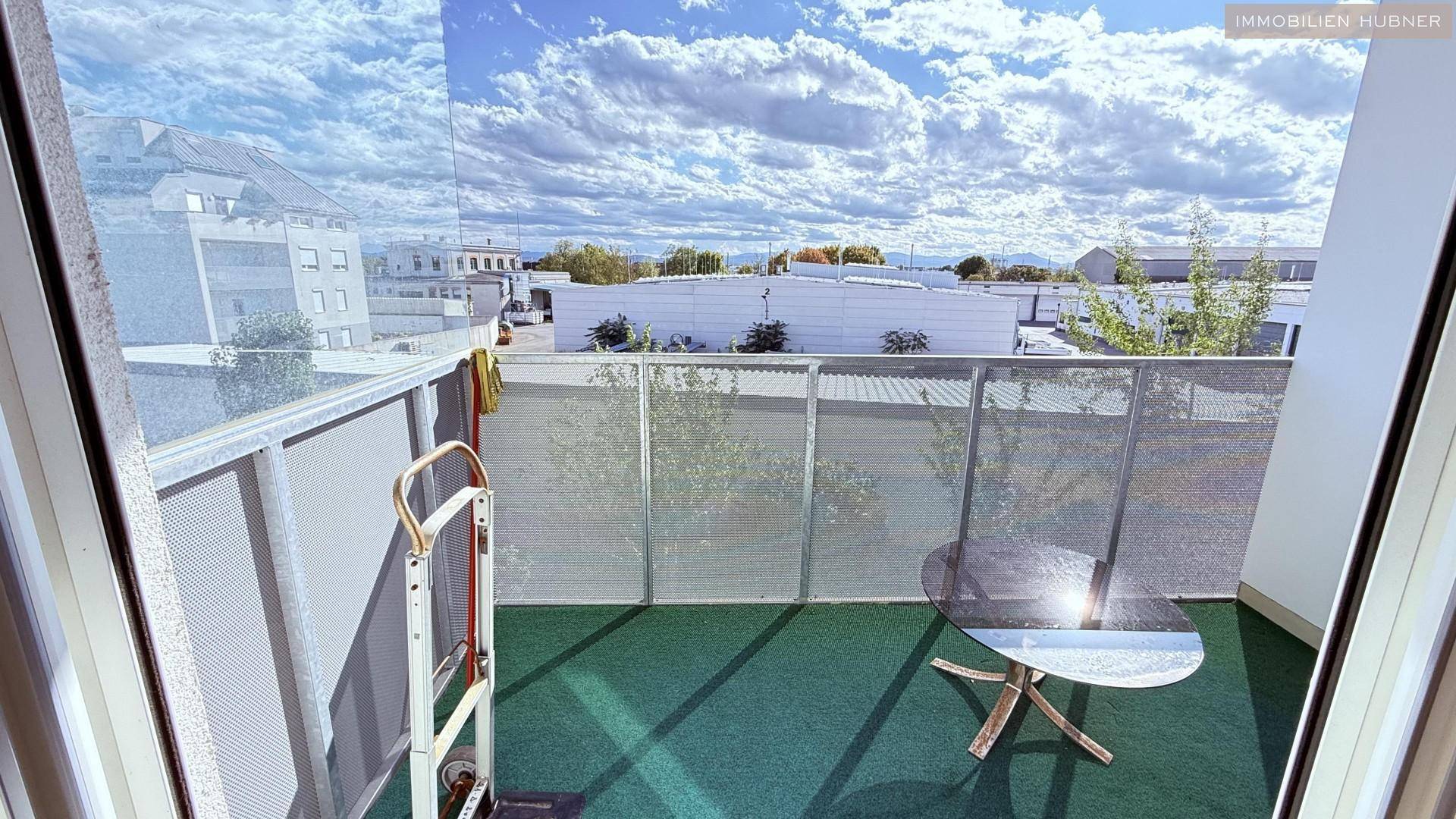 Kleiner Balkon mit Kunstrasen und einem Tisch, umgeben von anderen Gebäuden.