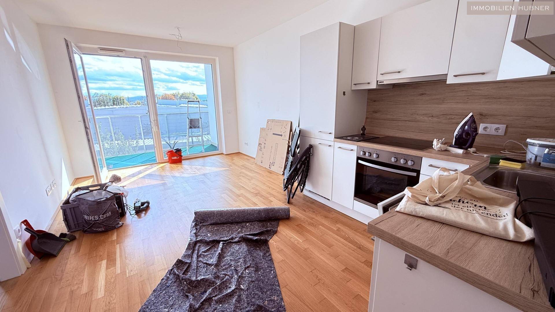 Heller offener Wohnbereich mit integrierter Küche, Parkettboden und Zugang zu einem Balkon.